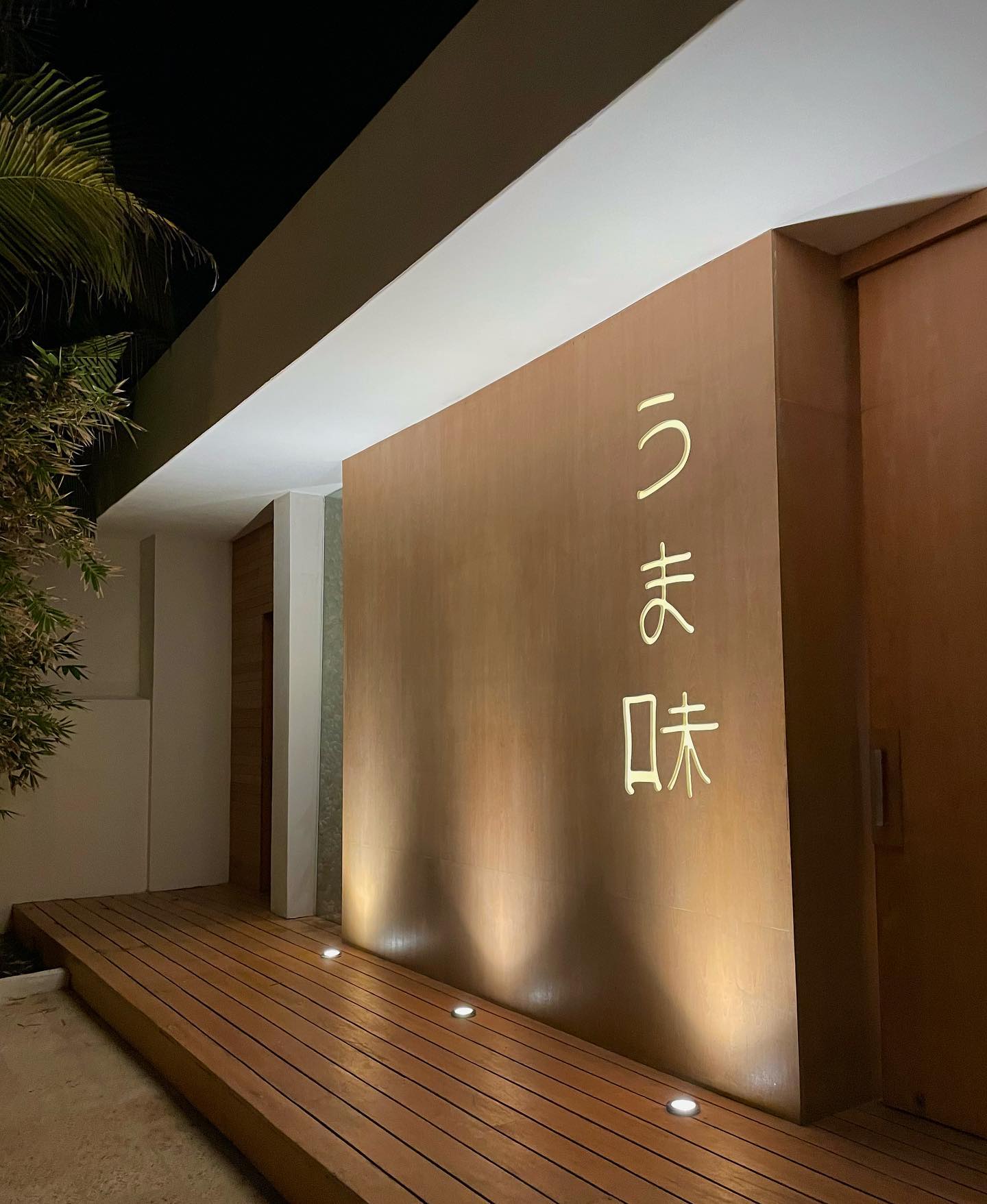 Warmly lit Umami restaurant entrance in Cancun, with vertical signage and a wooden walkway