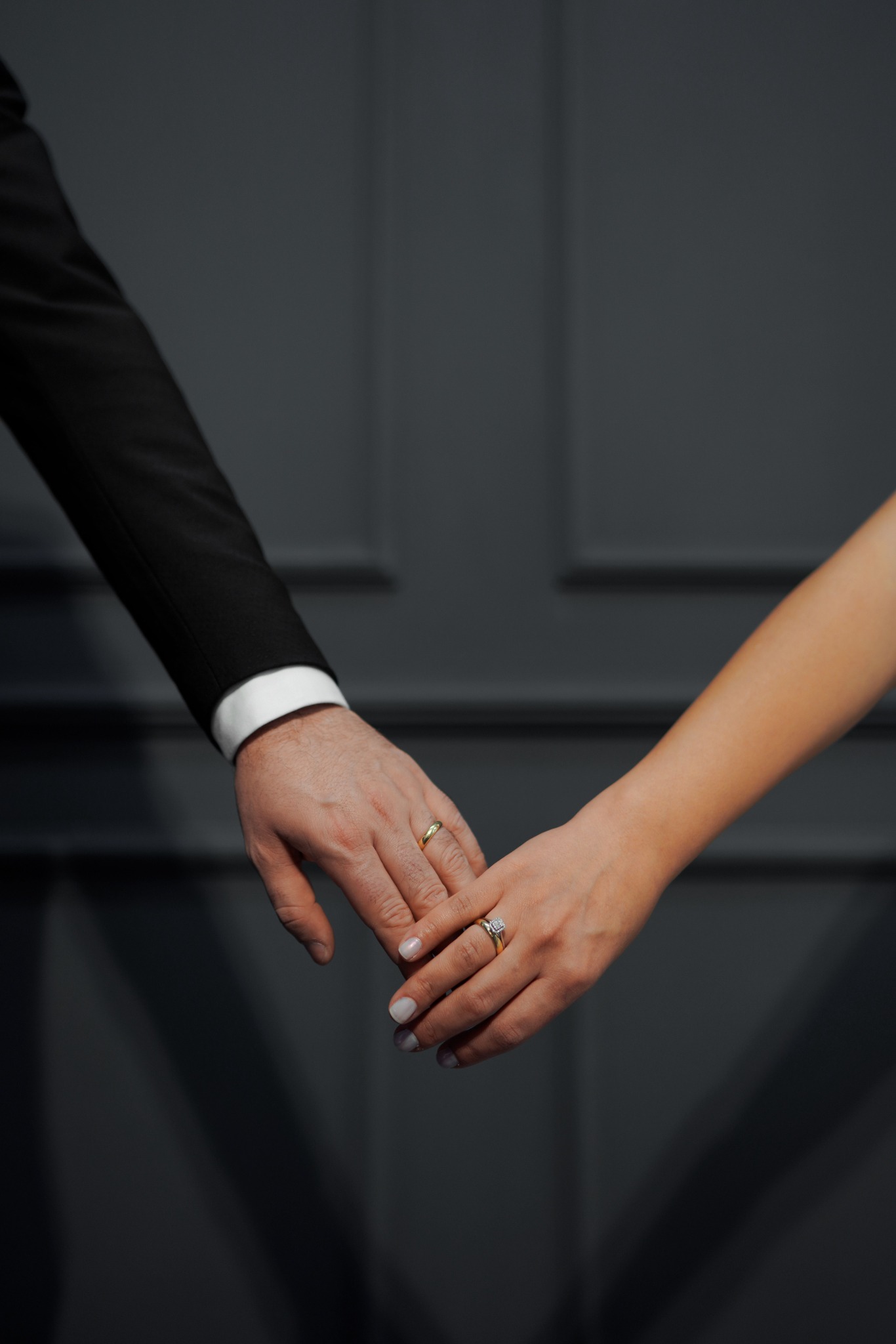 Close-up of a couple’s hands and wedding rings against a dark background