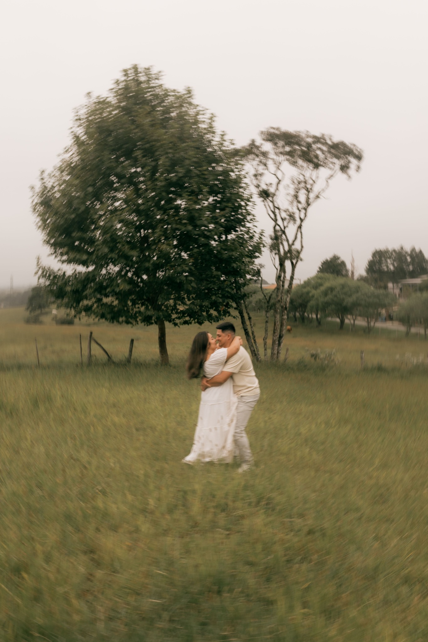 A couple embracing beneath trees in a meadow, surrounded by softly blurred grass
