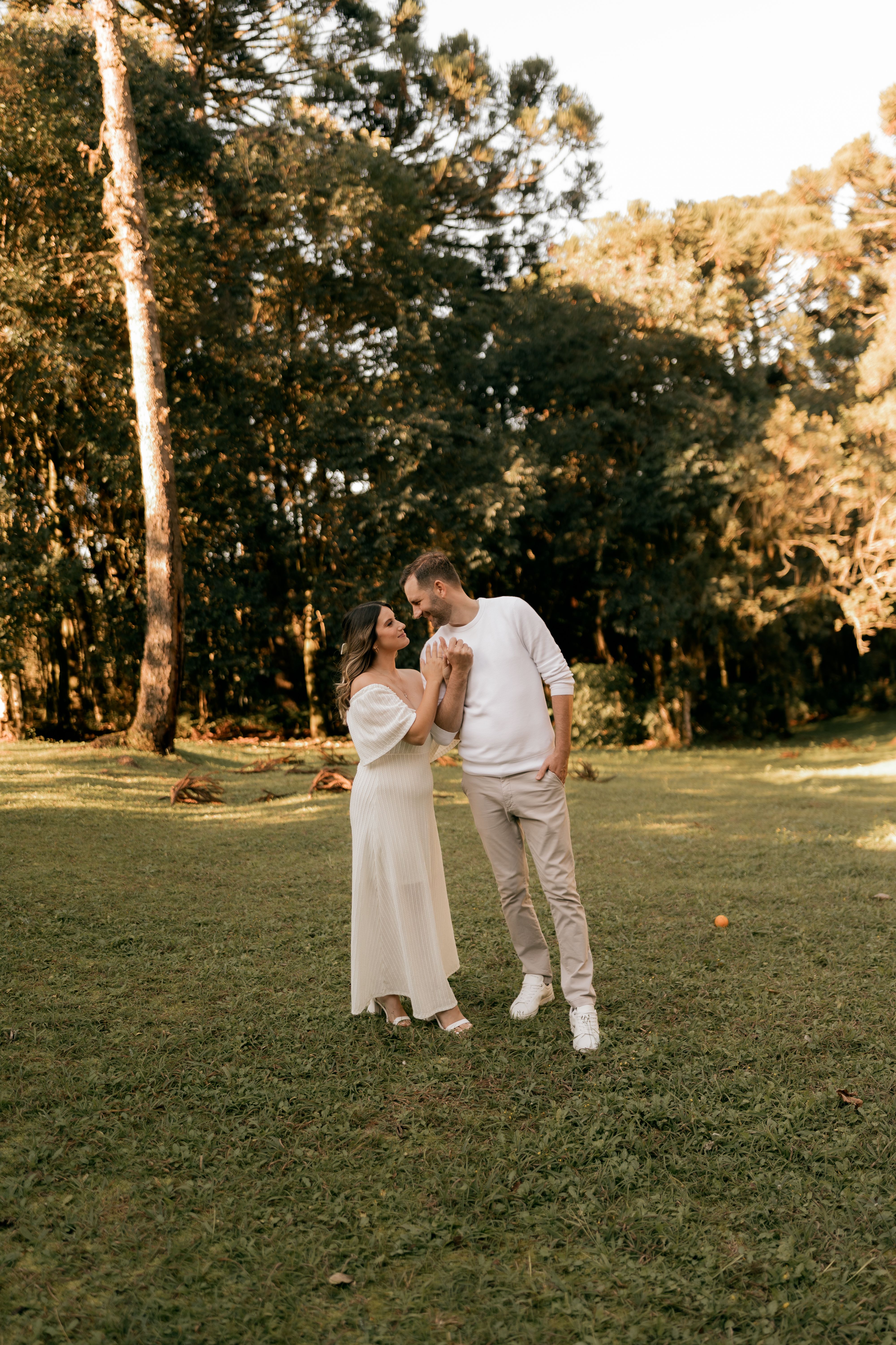 A couple holding hands and looking at each other in a sunlit woodland clearing