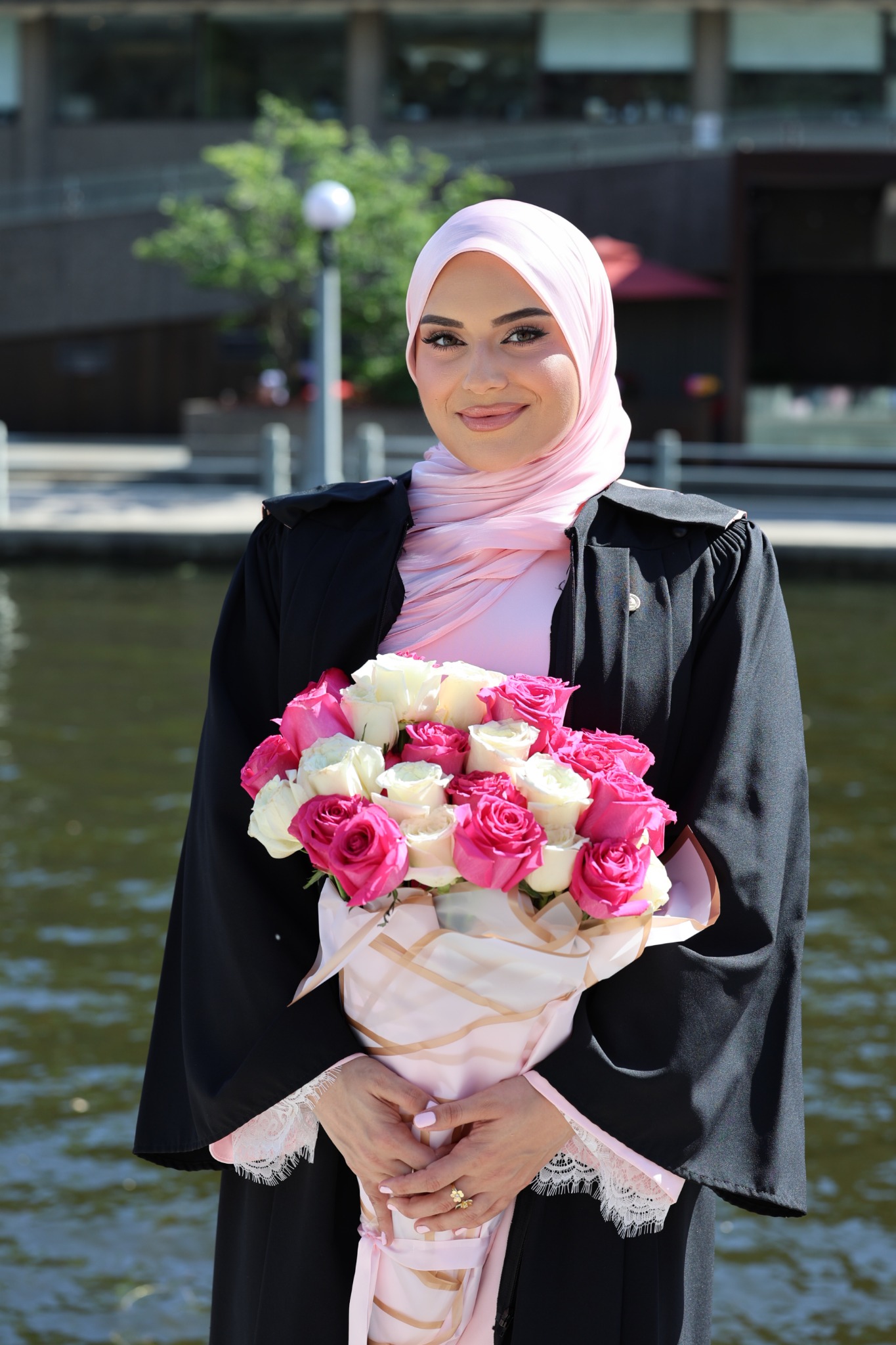 Graduate in a pink headscarf holding a bouquet by the water