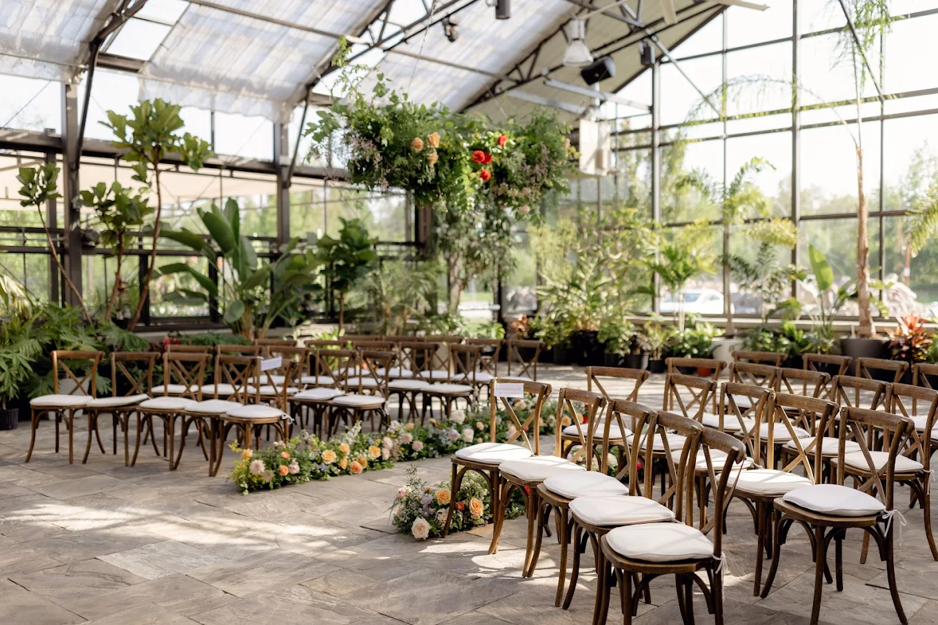 A sunlit greenhouse ceremony space with flowers and wooden chairs at Aquatopia