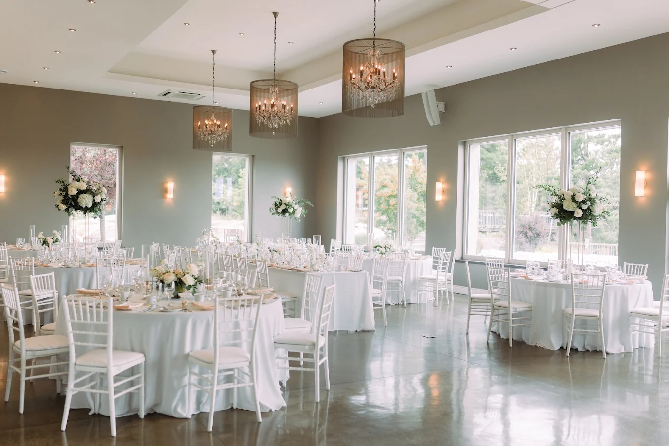 White wedding reception tables and floral arrangements beside tall windows at Le Belvédère